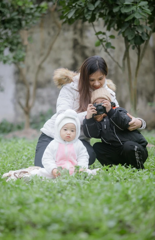 a woman and baby sitting in grass taking pictures