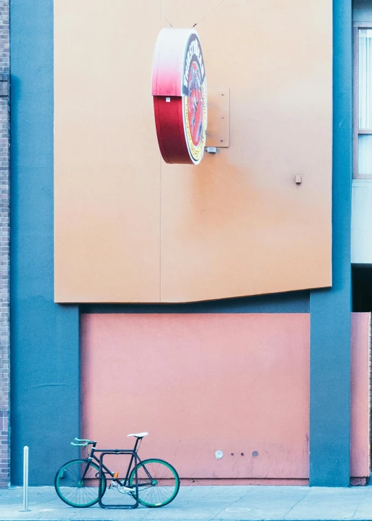 a bike parked near a yellow wall and a red clock