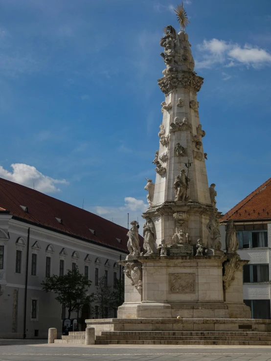 a tall structure with sculptures is shown in front of an old building