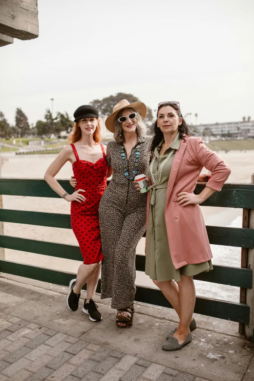 three ladies standing in front of the ocean near a wooden fence