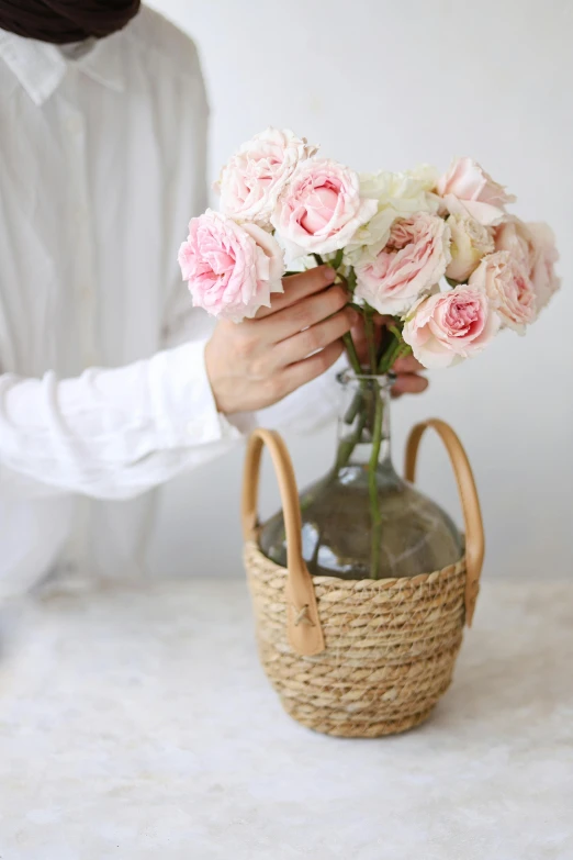 a person holding a wicker basket filled with pink roses