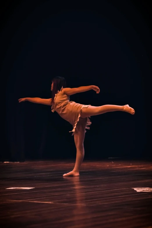 a female ballet student doing a dance move in the dark