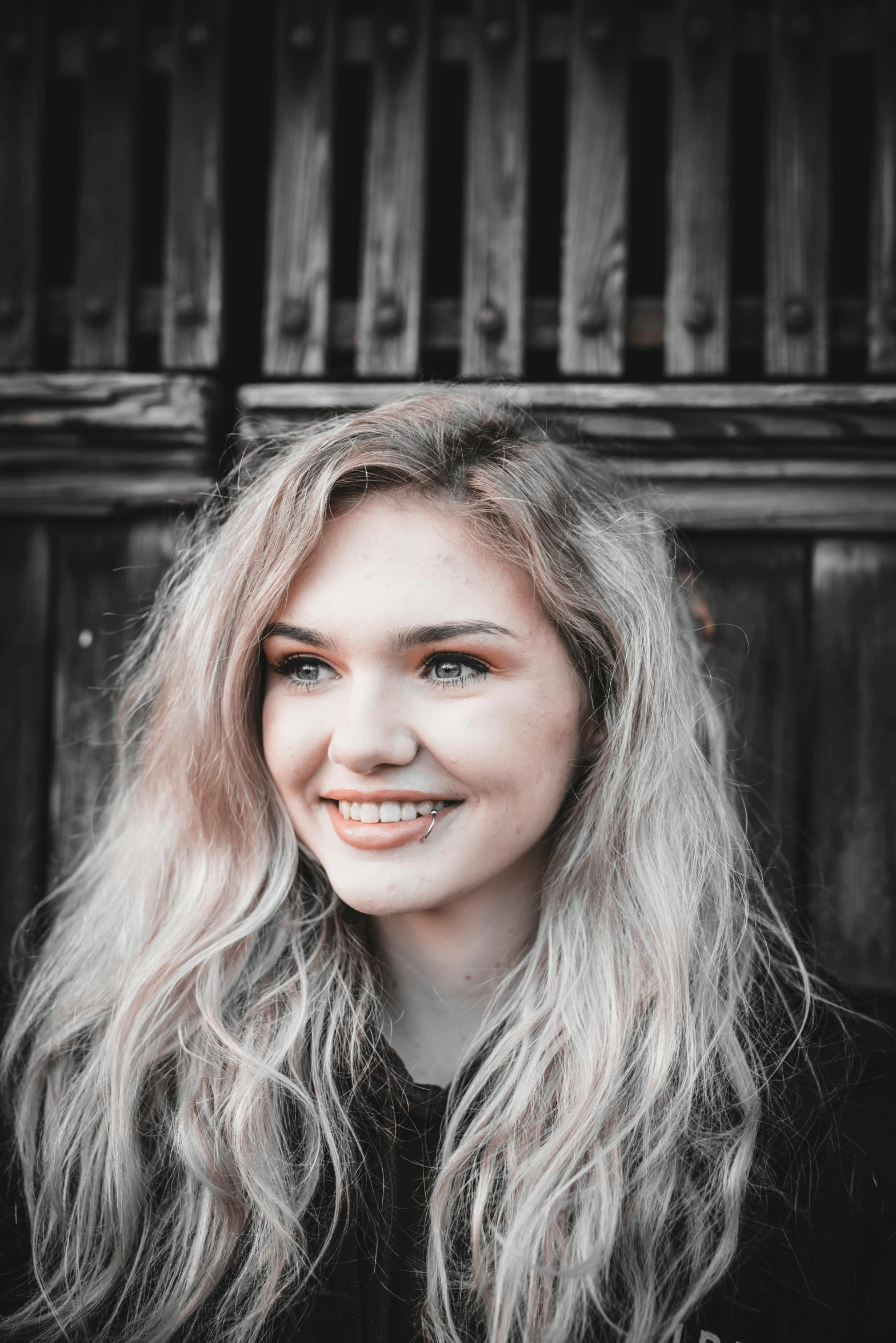 the girl is sitting in front of the wooden fence