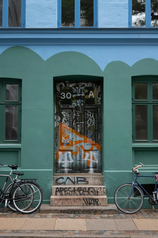 two bicycles sit in front of a door with graffiti