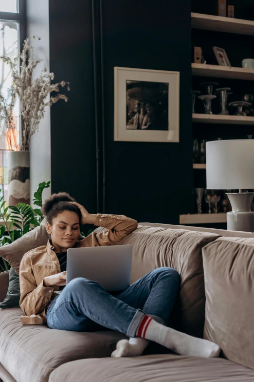 a woman sits on a couch working on a laptop