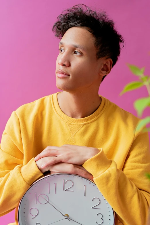 a young man wearing a yellow sweater holds an analog clock