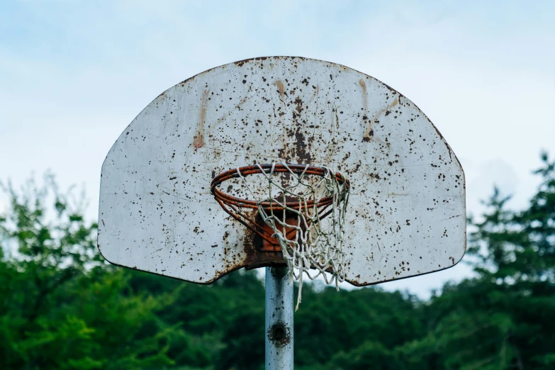 a broken basketball hoop sitting in front of some trees