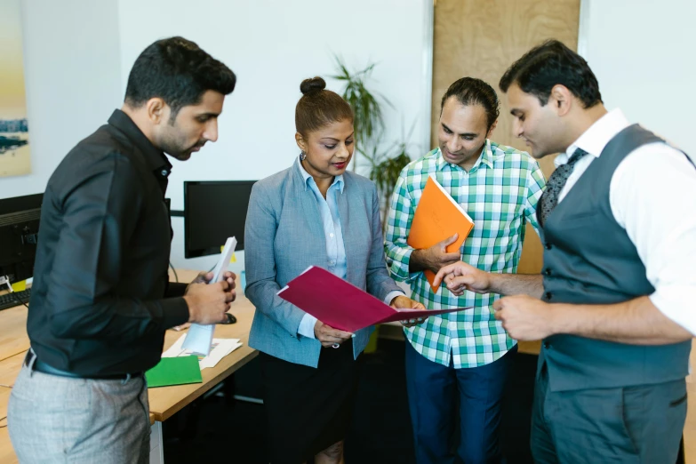 three men and one woman standing together in an office