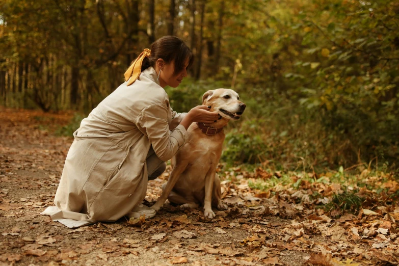 a woman is sitting down with a dog in the woods