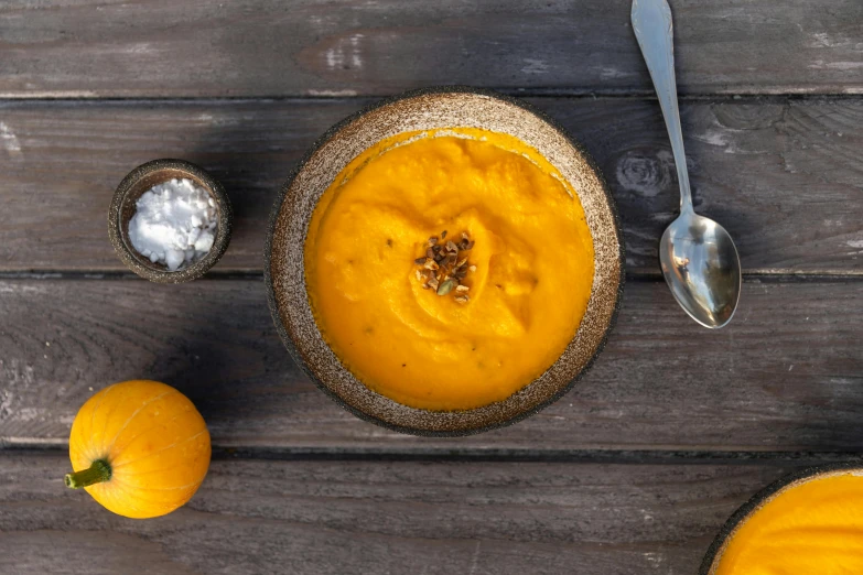 a table top with a bowl of pumpkin soup next to two spoons