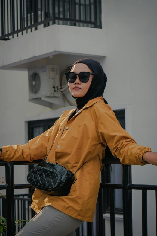 woman leaning on fence, wearing glasses and a head covering