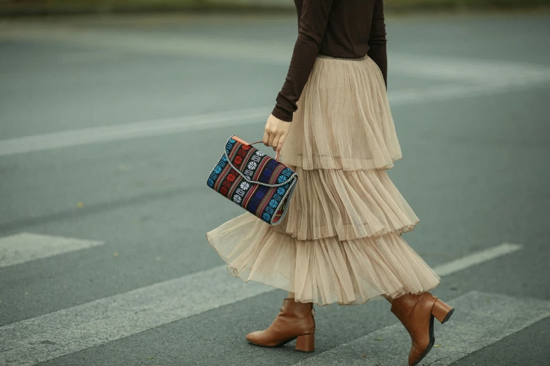 a woman in a tan pleated dress carrying a purse