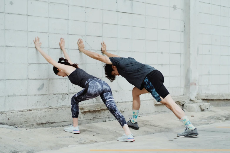 two women doing yoga outdoors in front of a wall