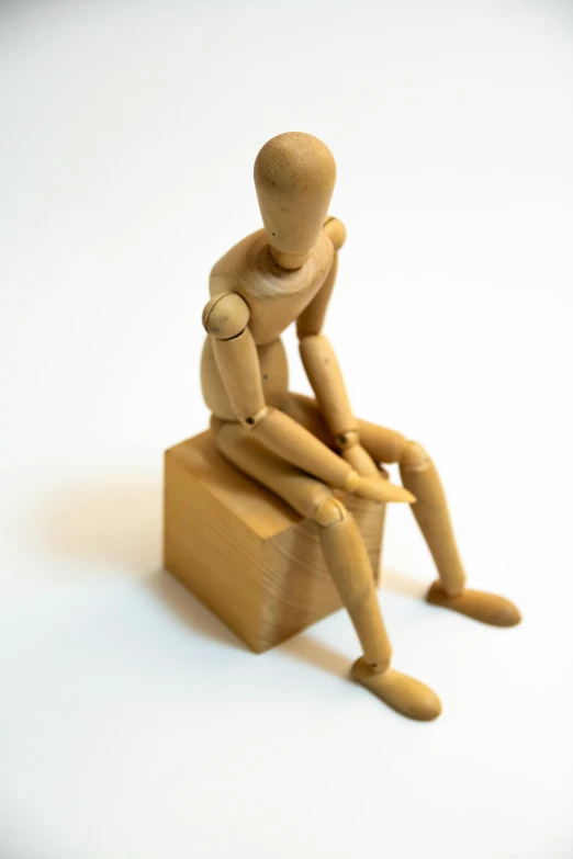 small doll sitting on a wooden block in a studio setting