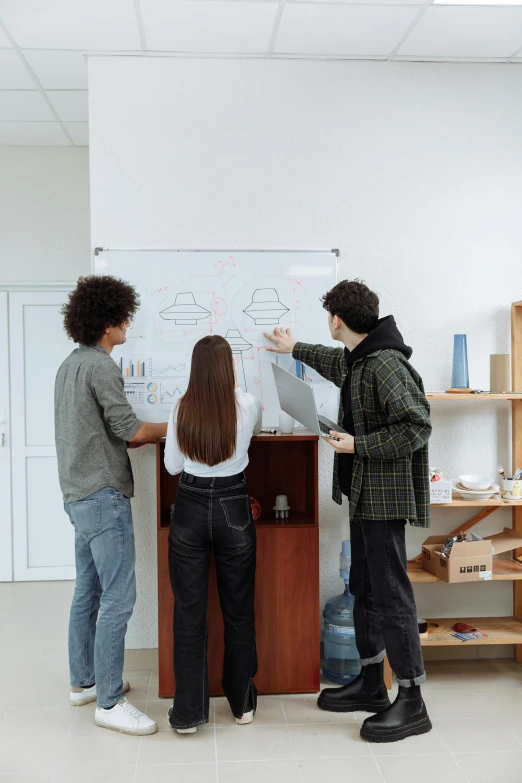 three people writing on a white board in front of shelves