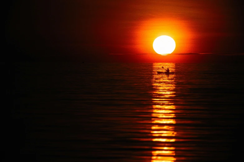 a lone boat in the water with a large sunset behind it