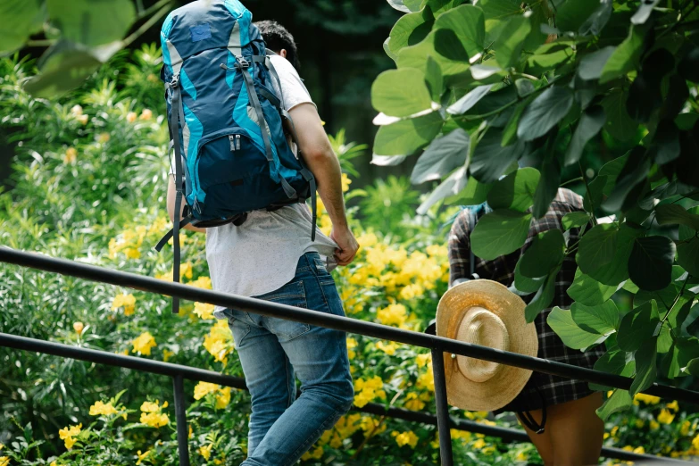 a man with a large backpack stands on a hand rail next to yellow flowers