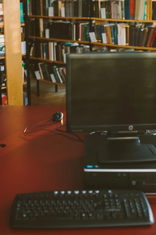 a computer, keyboard and mouse on a desk in front of bookshelves