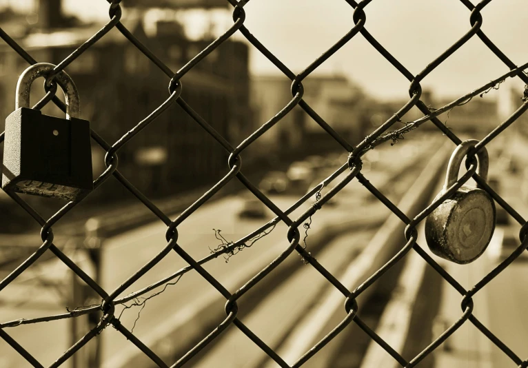 two locks attached to chain linked fence on train track