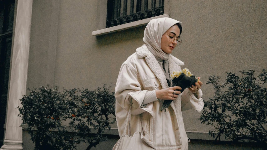 a person wearing a scarf holding flowers on the side of a building