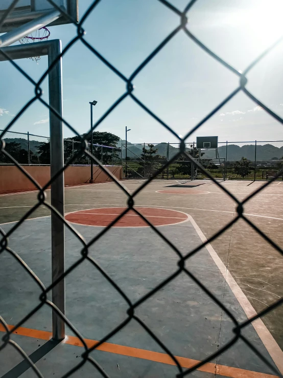 a basketball court seen through a fence with trees in the background