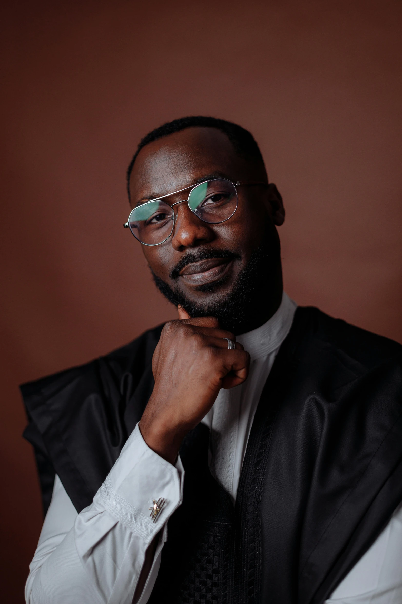 a man wearing glasses in front of a brown wall