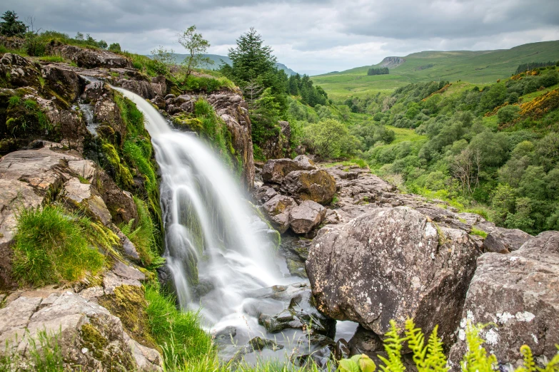 an outdoor waterfall surrounded by rocks, trees, and plants