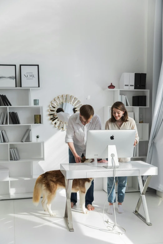 two young people look at a computer screen with their dog