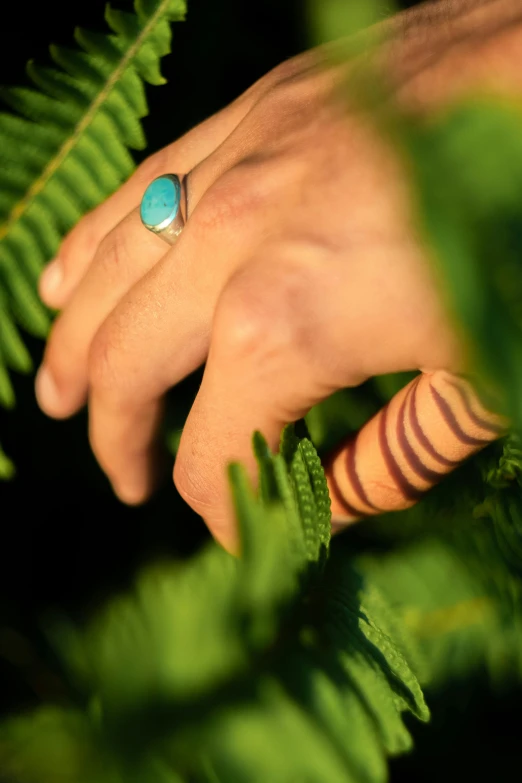 a person standing next to green leaf wearing a ring