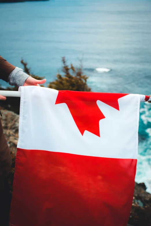 someone holding up an canadian flag with a body of water behind them