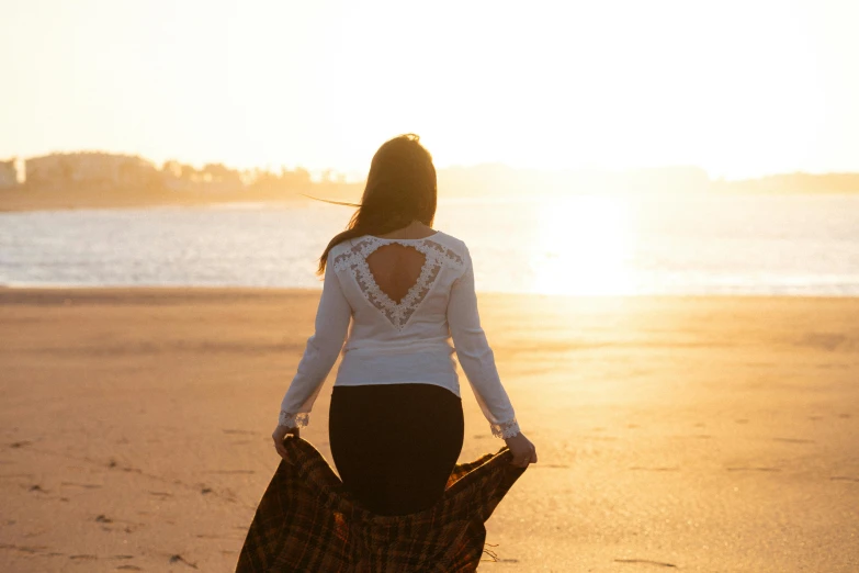 the back of a woman holding her purse standing on the beach