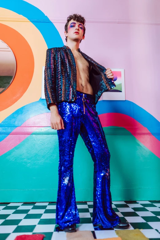 a man in bright blue sequin pants standing against a colorful wall