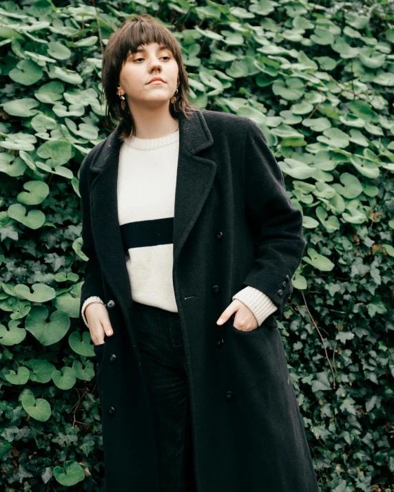 woman in black coat and sweater standing by bushes