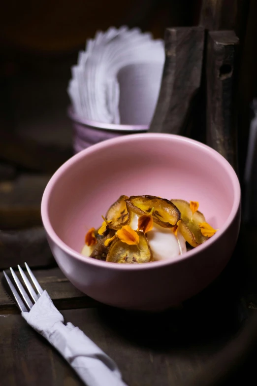 a pink bowl sitting on top of a table next to a silver fork