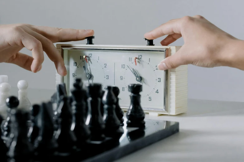two hands h the cover on a clock in a chess board game