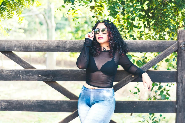 a woman posing for the camera leaning on a wooden fence