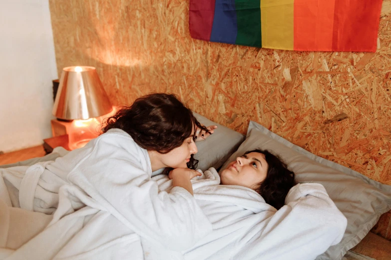 two women are laying in bed talking and having fun