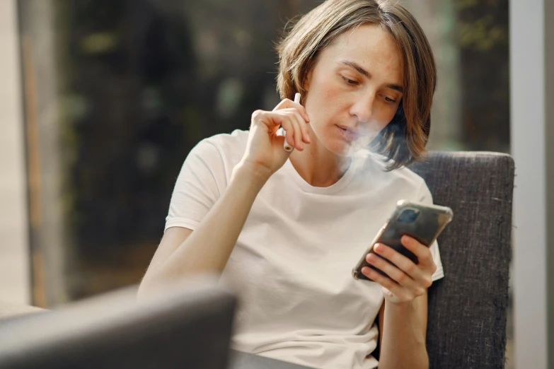 a woman sitting in an armchair smoking her cigarette and checking her cellphone