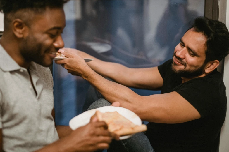 one person sitting and another man standing holding food in one hand