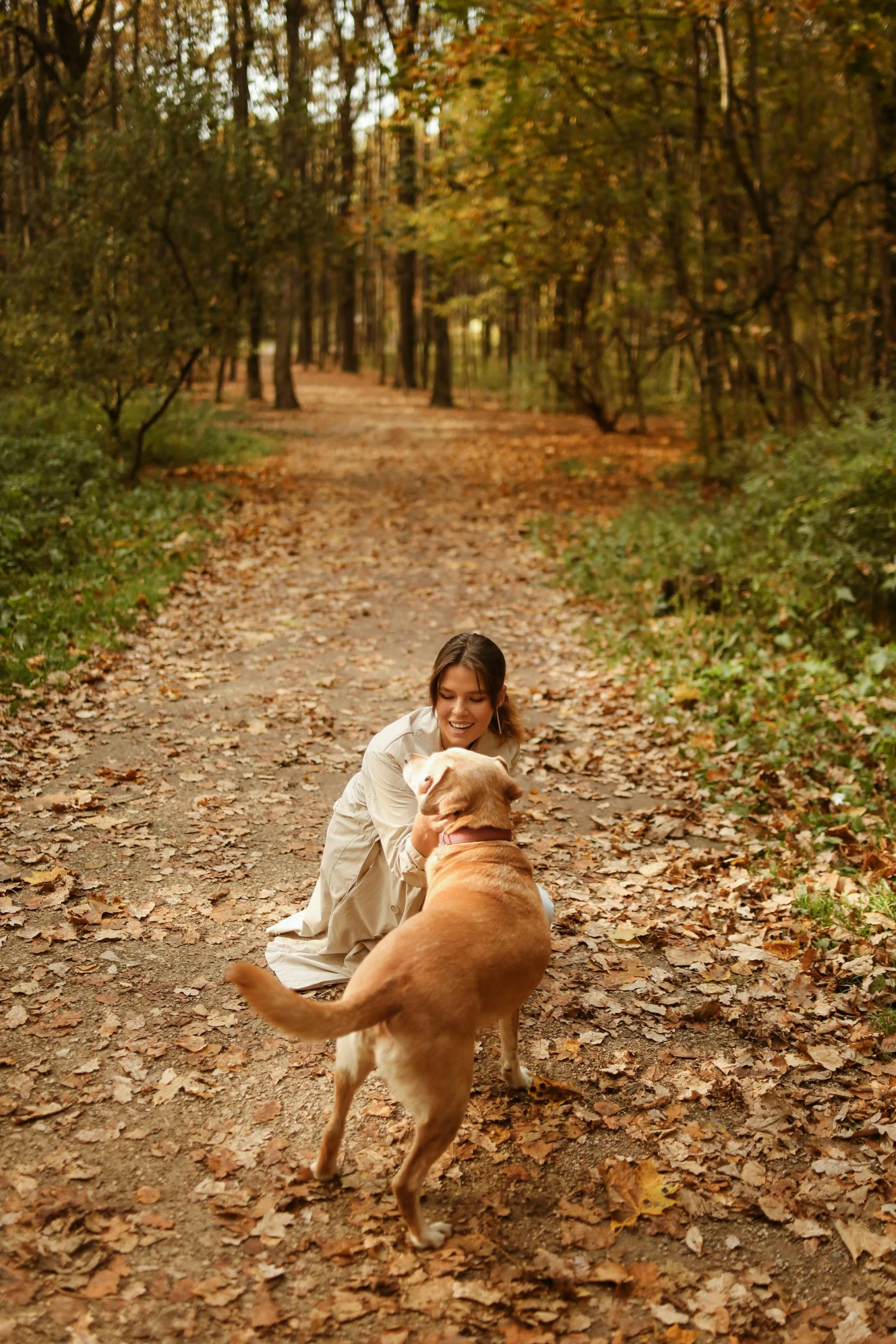 a woman kneeling on the ground with her dog in the middle of a leaf covered path