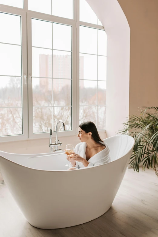 a woman sitting in a white tub with two wine glasses