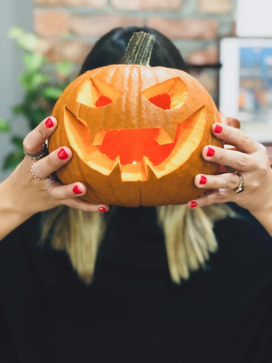 a woman holding up a carved pumpkin for a scary face