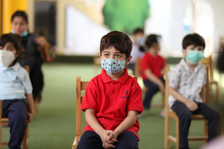 a group of children in red shirts sit with their faces masks on