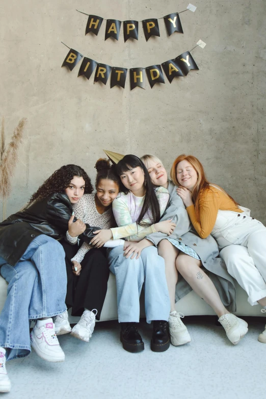 five women pose on a white couch with a happy birthday banner