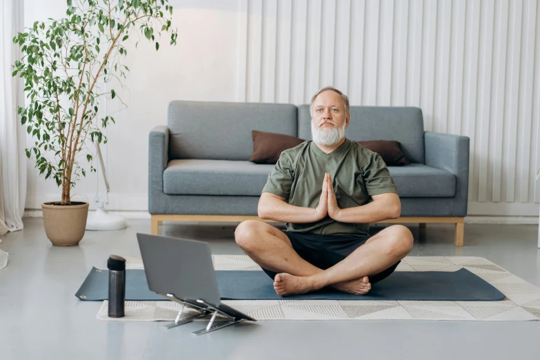 a man sits on a mat while using his laptop