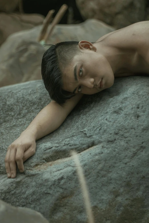 shirtless young man resting his head on the rock