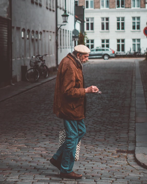 an old man walking down a brick street while looking at a cell phone