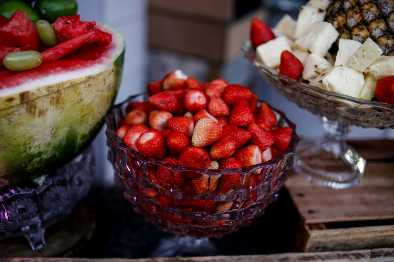 a watermelon slice sitting next to a glass bowl filled with strawberries and other fruits