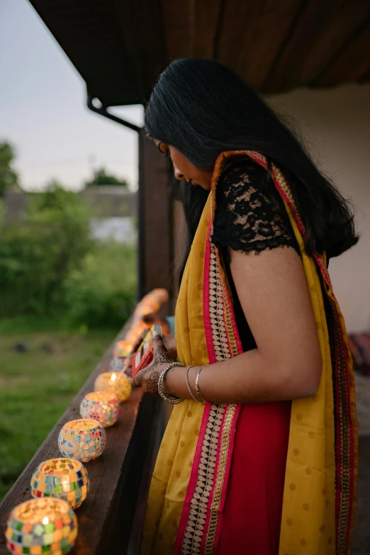 woman lighting brightly colored lamps for diwals at the end of an outdoor walkway