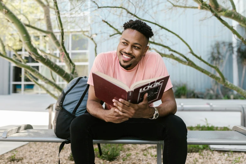 a smiling guy is sitting on a bench reading a book